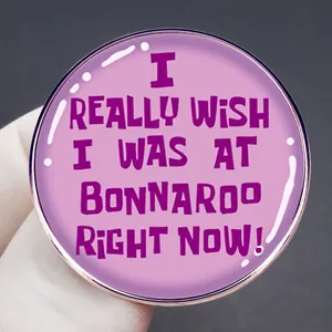 Pink enamel Bonnaroo music festival lapel pin with purple text slogan held in hand