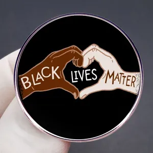 Κυκλική μεταλλική κονκάρδα Black Lives Matter με χέρια σε σχήμα καρδιάς σε γκρίζο φόντο