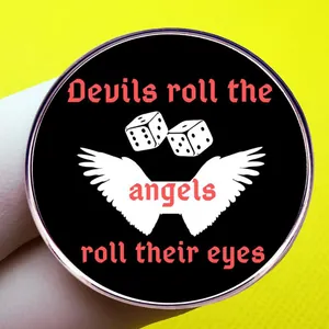 Round enamel pin featuring wings, dice and Devils roll the dice angels roll their eyes text