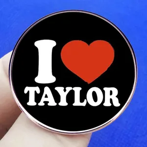 Badge rond en métal 'I Love Taylor' avec cœur rouge tenu sur un fond bleu avec texture