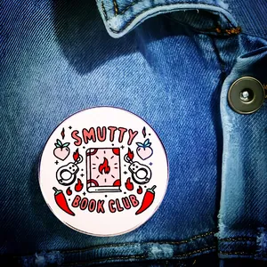 Close-up of Smutty Book Club enamel pin displayed on a dark blue denim jacket