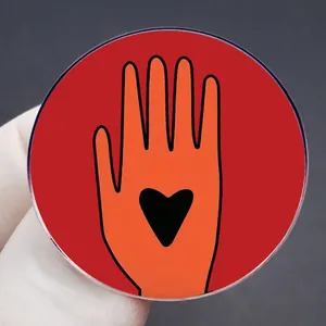 Close-up of acrylic Ceasefire brooch badge with orange hand and black heart on palm