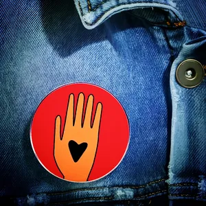 Detail of Ceasefire hand badge with heart pinned on a denim jacket pocket