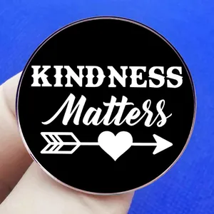 Round Kindness Matters enamel brooch pin with heart arrow design on black background