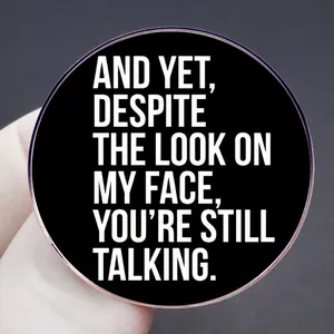 Black round sarcastic quote brooch: And yet despite the look on my face you are still talking