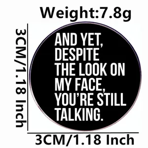 Black round sarcastic pin badge: And yet, despite the look on my face, you are still talking