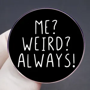 Dettaglio macro della spilla tonda in metallo con testo bianco 'ME? WEIRD? ALWAYS!'