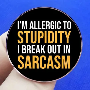 Enamel pin badge with I'm Allergic to Stupidity quote held against a blue background