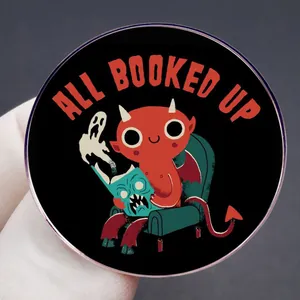 Badge All Booked Up avec petit démon rouge lisant un livre sur fond sombre élégant