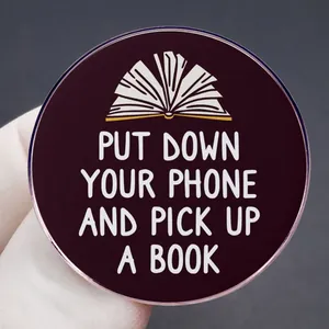 Round purple enamel pin with white lettering Put Down Your Phone and Pick Up A Book