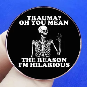 Black round enamel pin with skeleton and trauma joke text on a blue background