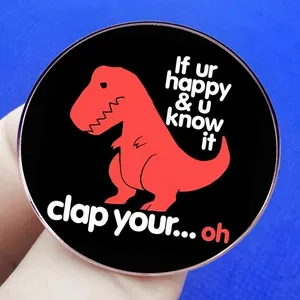 Round black enamel T-Rex pin with humorous 'If ur happy and u know it clap your hands' text