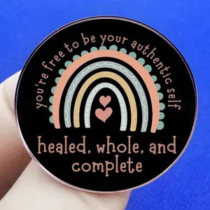 Black round inspirational brooch with rainbow design and rose gold edge on blue fabric