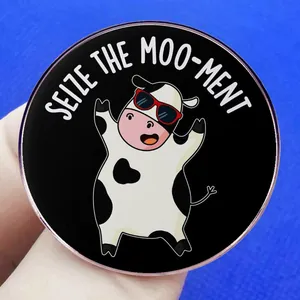 Spilla a forma di mucca cartoon con scritta 'SEIZE THE MOO-MENT' su sfondo blu
