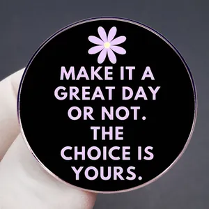Broche en émail noir mat avec motif marguerite et citation inspirante tenue par la main