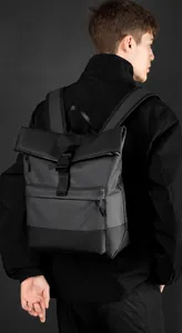 Rear view of model wearing a black waterproof business backpack with flap buckle and matte finish
