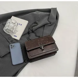 Detail of dark brown leather chain bag with oily texture on a grey blazer