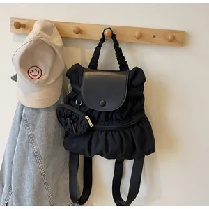 Detail of black pleated nylon backpack with mini round pouch hanging on a wooden hook