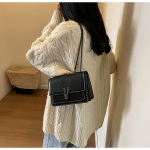 Detail of a black vintage crossbody bag with white contrast stitching on a beige sweater