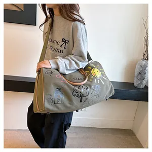 Détail du sac de voyage en toile vert armée avec graffiti et large bandoulière