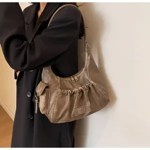 Close-up of pleated brown shoulder bag detail with side pocket and metallic zipper