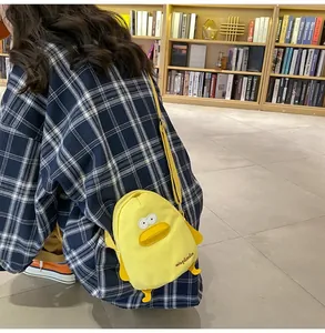 Detailed view of the yellow duck canvas crossbody bag worn by a model in a library