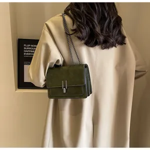 Detail of dark green suede-textured crossbody bag with silver chain and metal clasp