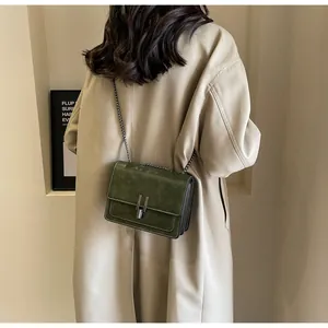 Detail of dark green retro crossbody bag with metallic chain strap worn by a model