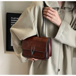 Close-up of vintage brown crossbody bag with metal chain strap and vertical buckle lock