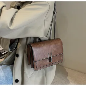 Detail of vintage brown leather chain bag with metallic clasp worn with beige trench coat