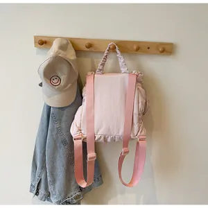 Detailed view of pink nylon backpack with ruffle trim on wooden hanger and denim jacket