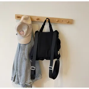 Detail of black pleated nylon backpack with ruffled straps hanging on a wall hook