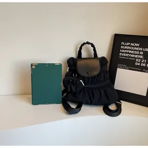 Detailed macro view of black nylon backpack featuring ruffle design and faux leather flap