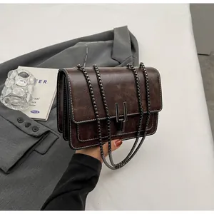 Detailed close-up of a vintage brown crossbody bag with metal chain and dual lock texture