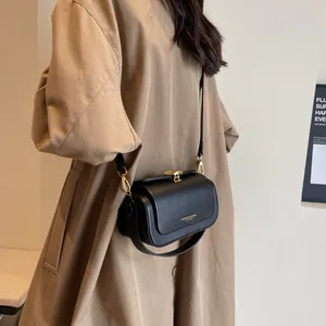 Elegant black leather crossbody bag with gold bow clasp on a model in a khaki trench coat