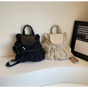 Detail of pleated nylon backpacks in black and beige with matching mini purse charms