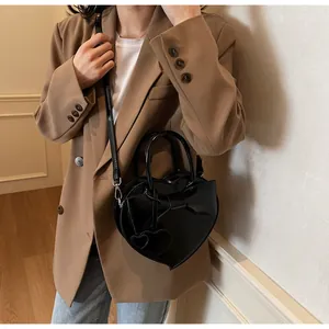Modella che indossa una borsa nera a forma di cuore con fiocco e tracolla sottile