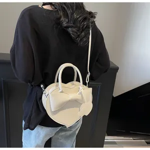 Borsa a tracolla bianca a forma di cuore con fiocco indossata da una persona da dietro