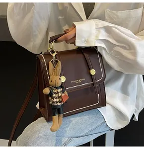 Detalle de un bolso de cuero marrón oscuro con bordes perlados y un colgante de conejo