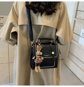 Detalle de bolso bandolera negro con colgante de conejo y costuras onduladas en gabardina