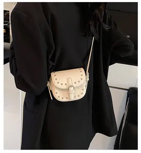 Detail view of cream saddle bag with silver rivets worn by a model in a black blazer