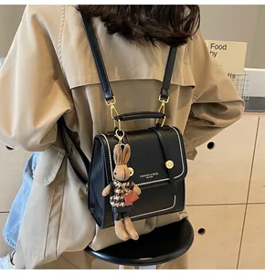 Detalle de mochila de cuero PU negro con costuras blancas y colgante de conejo sobre gabardina