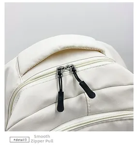 Close-up of the reinforced handle and smooth double zipper pull on the beige backpack