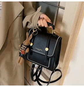 Detalle de mochila de cuero negro con costuras blancas y colgante de conejo