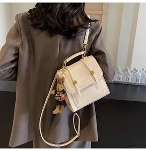 Detalle del bolso convertible crema con hebillas doradas y colgante de conejo de peluche
