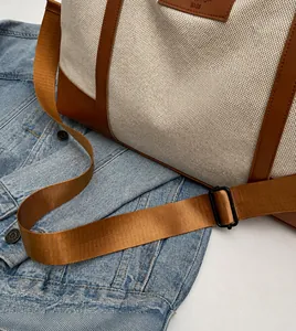 Detail of adjustable nylon shoulder strap and brown leather trim on canvas travel bag