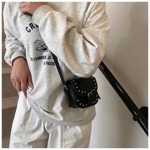 Close-up of a black leather mini saddle bag with silver studs on a model in a stairwell