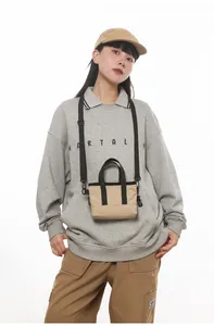 Close-up of mini khaki canvas tote bag with black straps on a casual streetwear model
