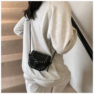 Mini black saddle crossbody bag with silver studs worn by a model in a casual setting