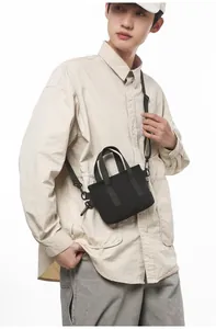 Detail of a minimalist black canvas crossbody bag with dual handles and nylon shoulder strap